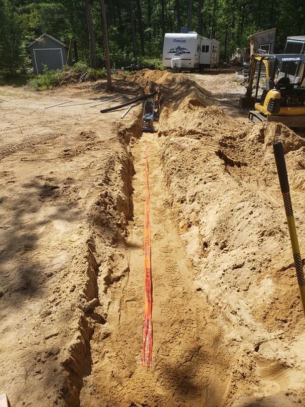 Trench dug in sandy soil with orange conduit; small shed and RV in the background.