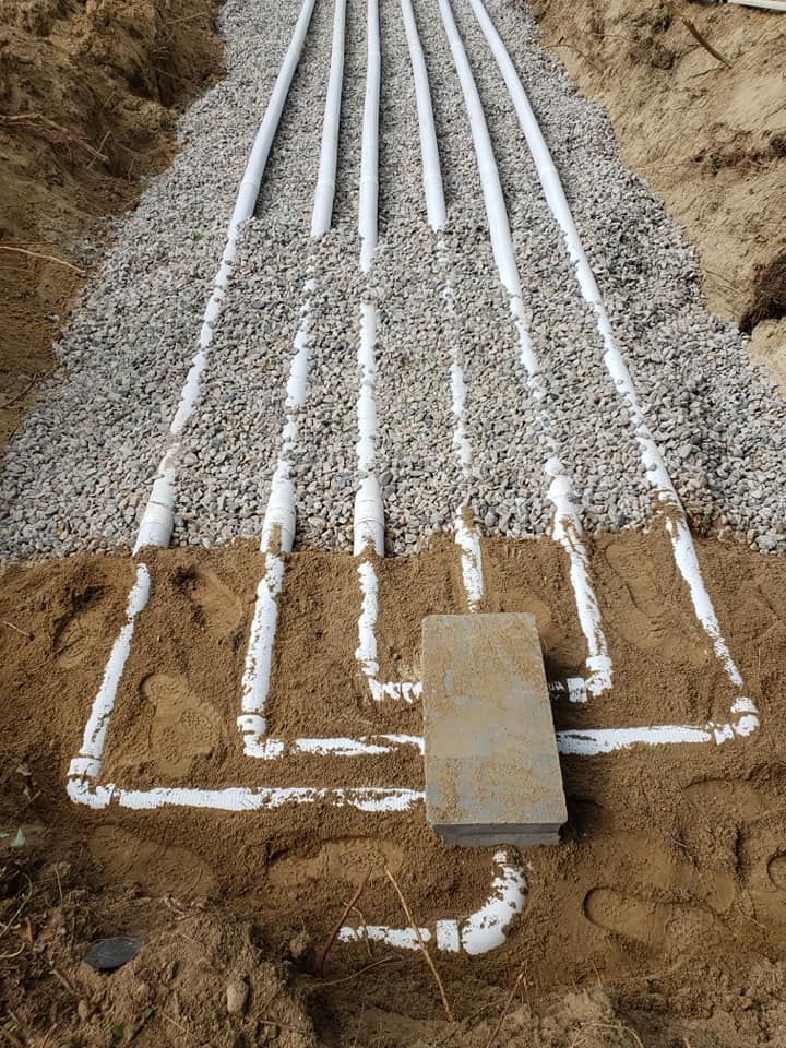 A septic system drain field under construction: white pipes in gravel and sand.