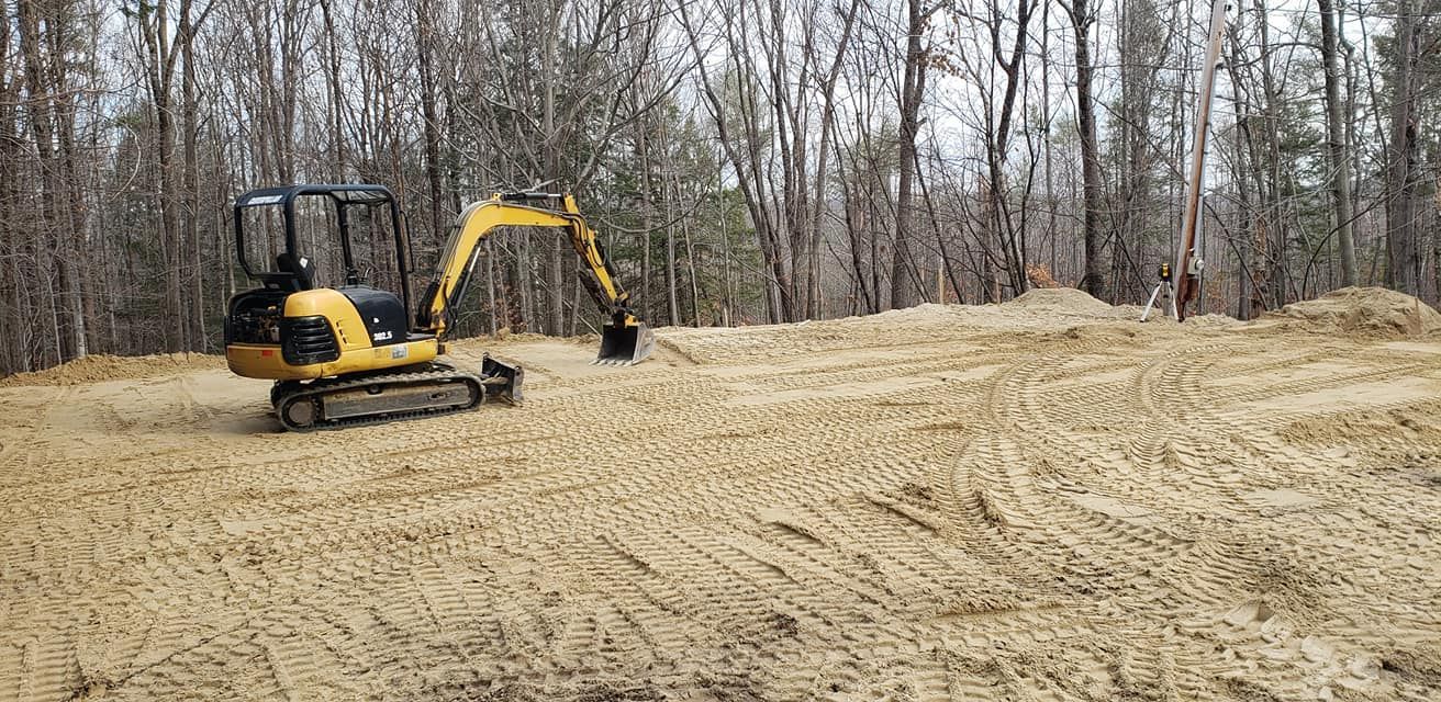 A yellow excavator on a sandy, cleared area in a wooded setting.