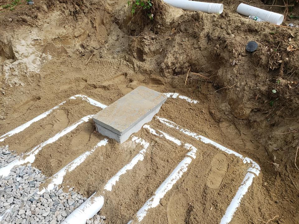 A white septic drain field being installed in a sandy trench, with gravel and a concrete block.