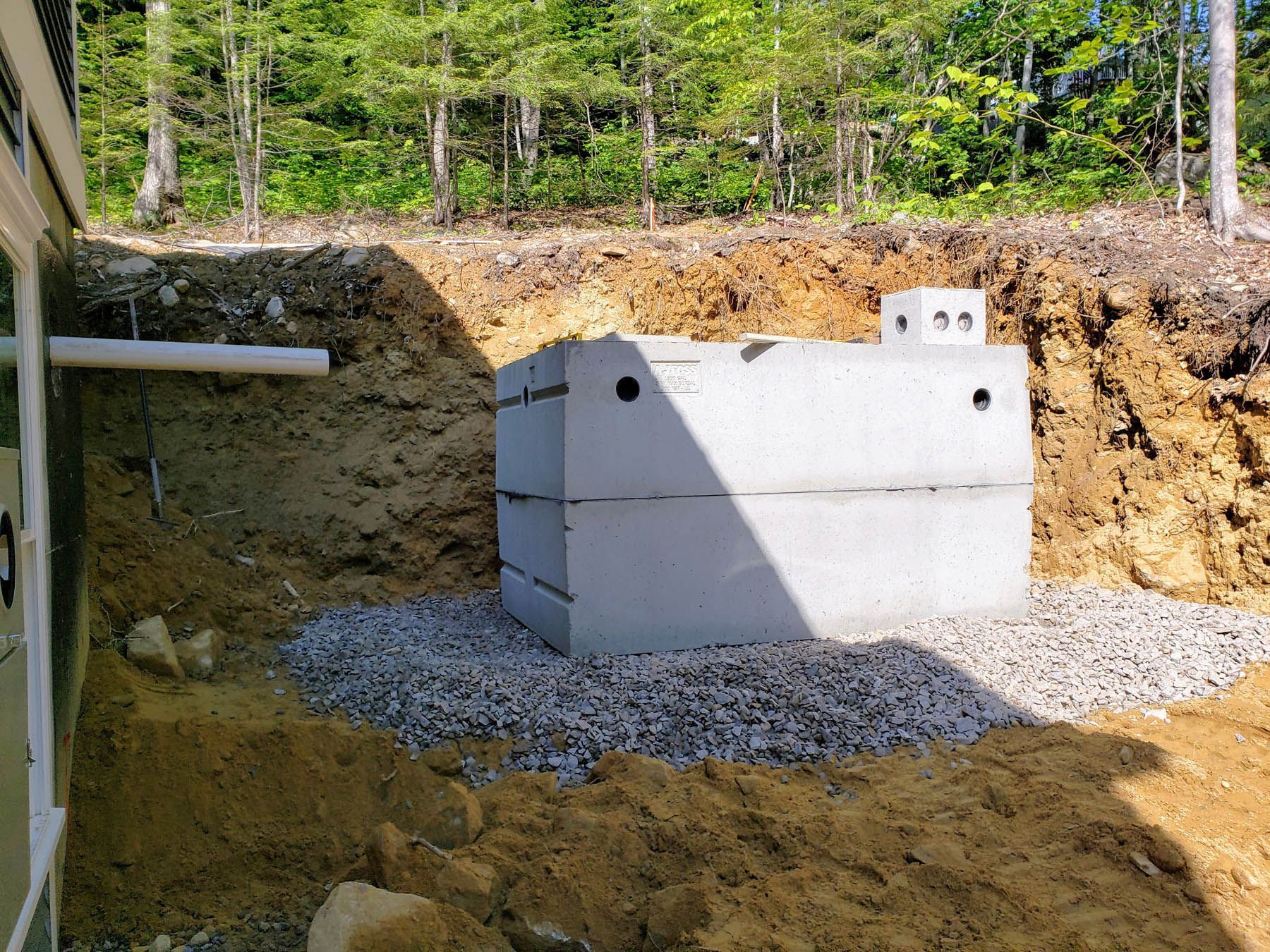 Concrete septic tank installed next to a house and hillside, surrounded by gravel.