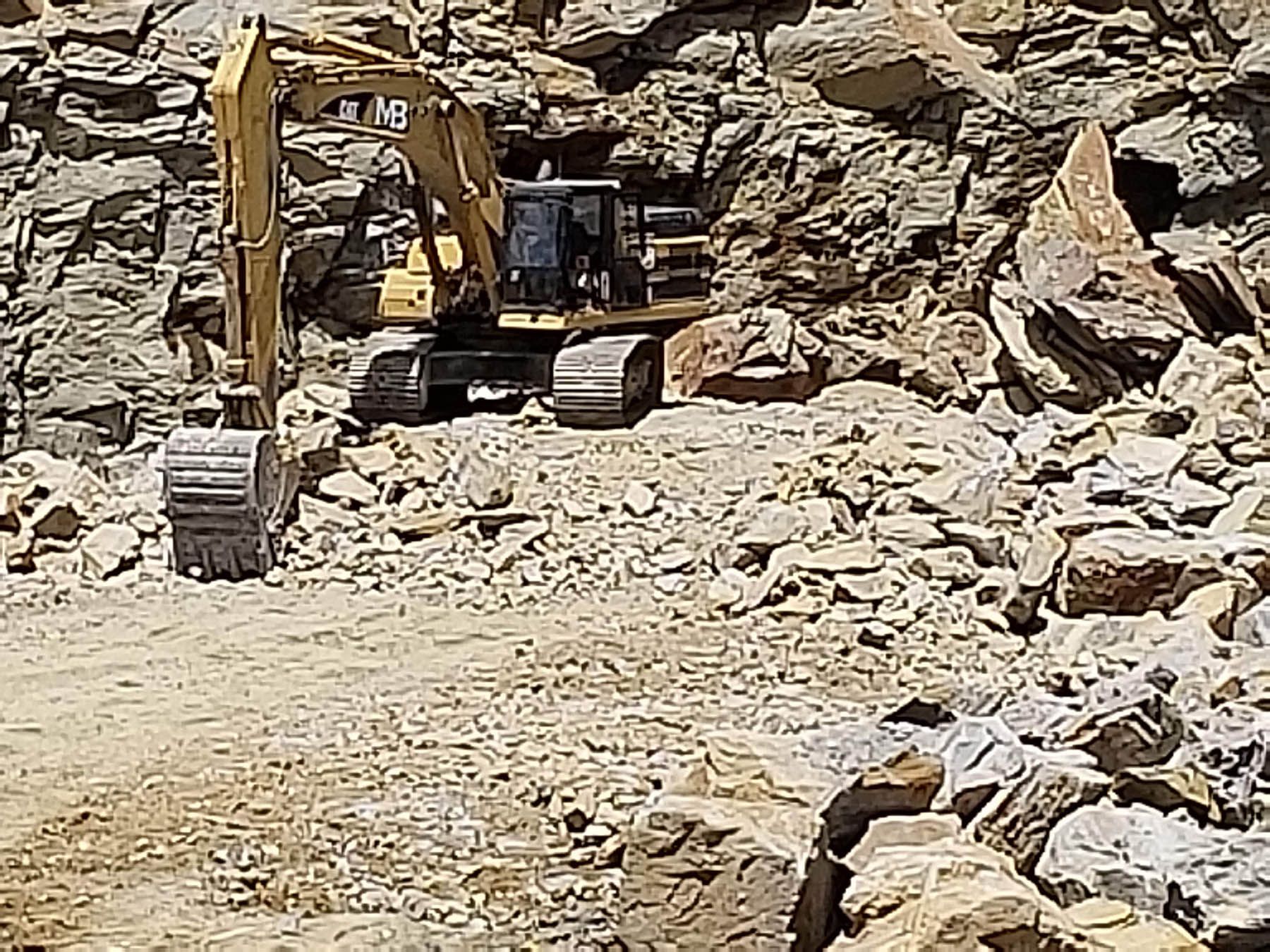 Yellow excavator in a rocky quarry.