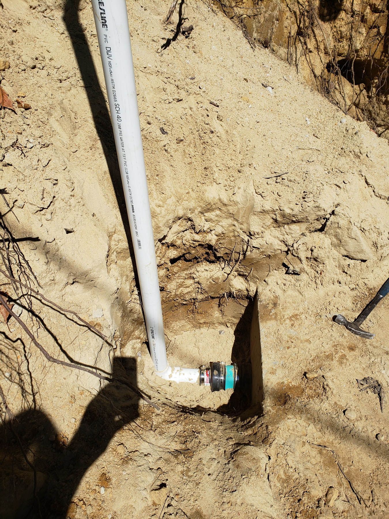 White PVC pipe and fitting installed in a trench in sandy soil; construction scene.