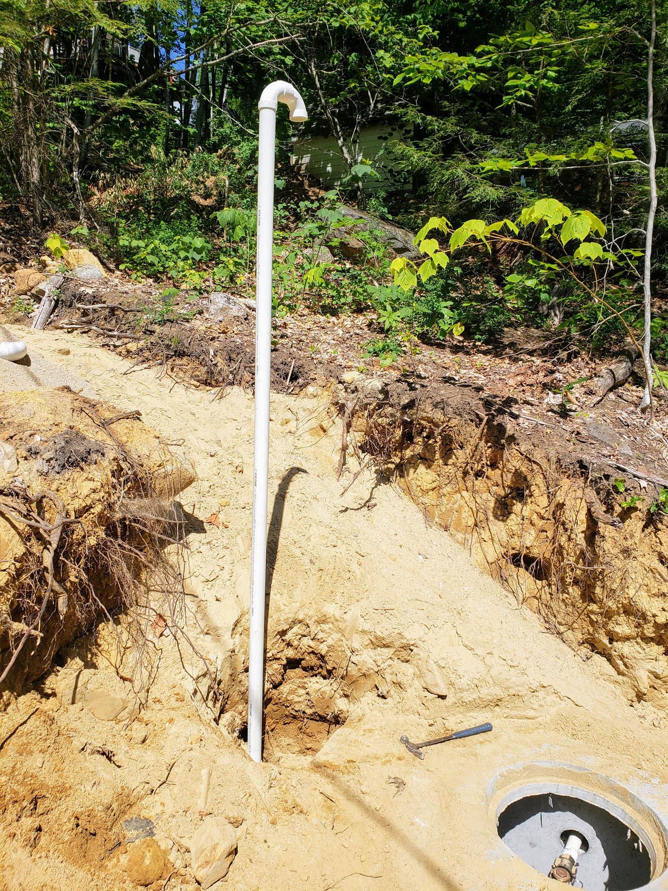 White PVC pipe with curved top, installed in sandy soil near a well.