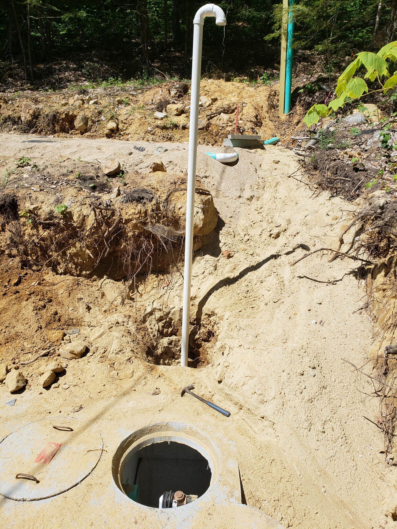 Open well with white pipe extending upwards, surrounded by excavated sand and dirt.