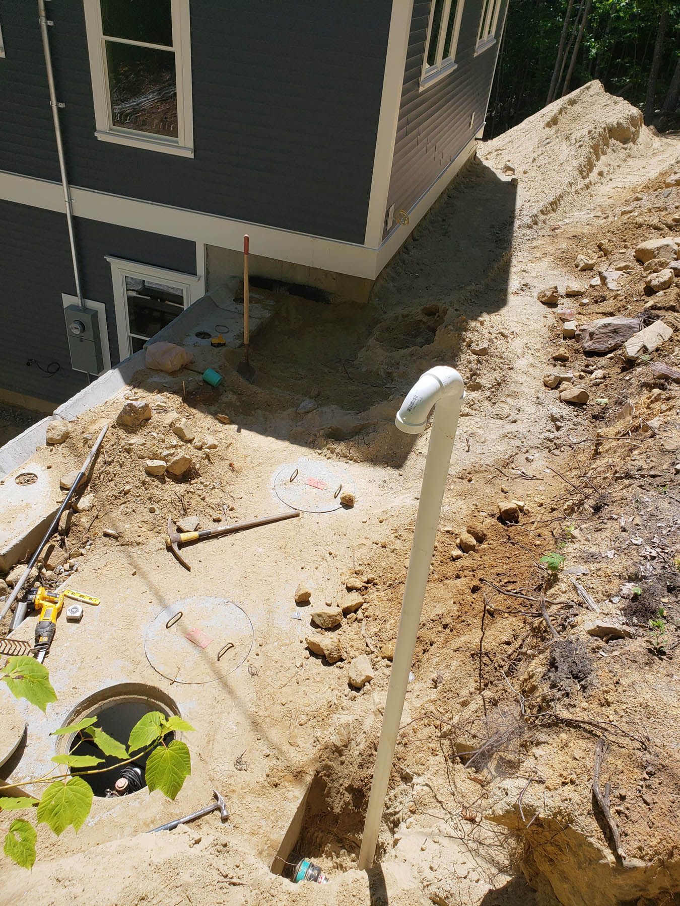 Construction site with trenches and a building. Earth-toned dirt, white pipe, and blue siding.