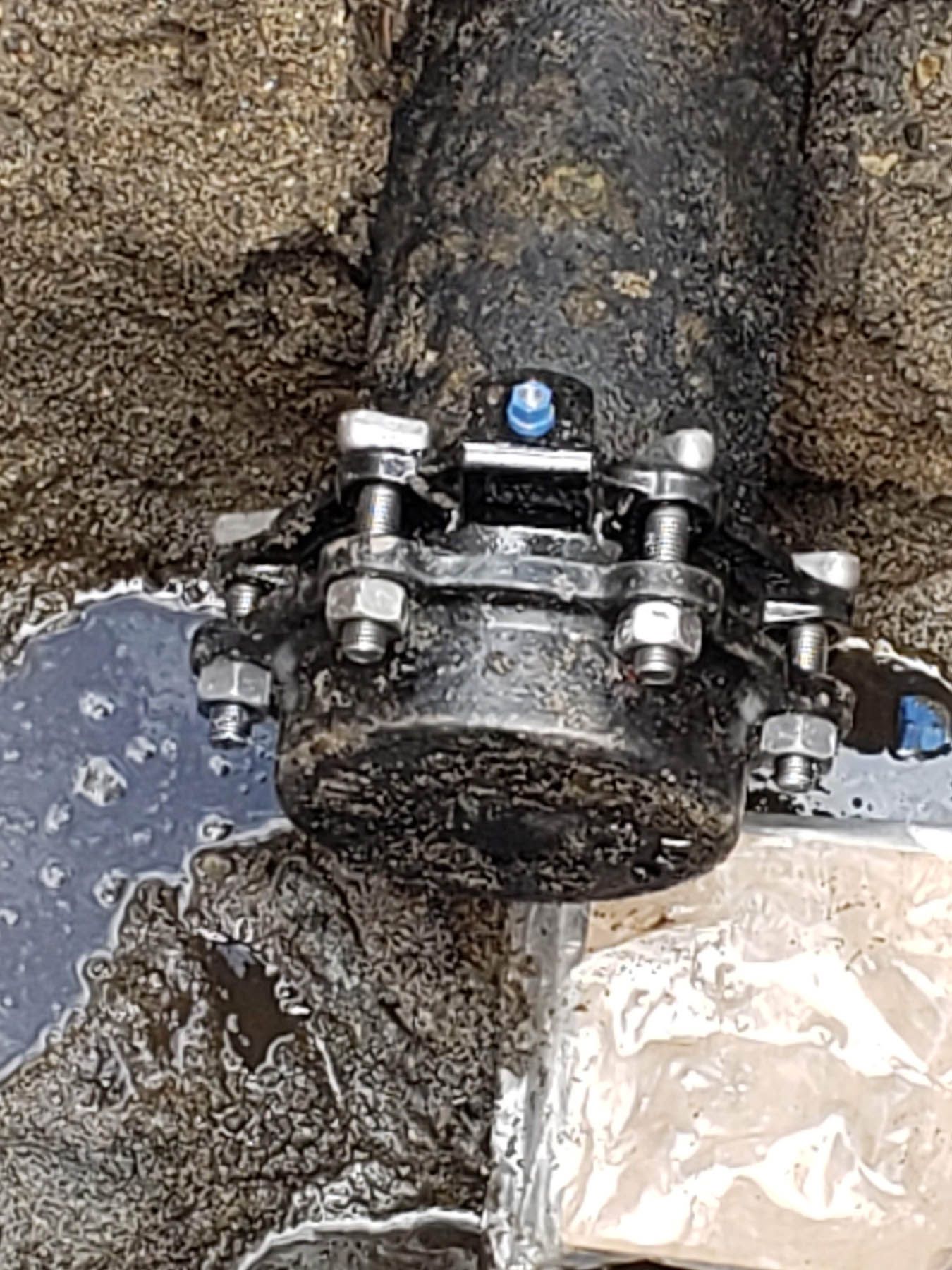Black pipe joint with bolts and a blue marker in a wet, dark setting.