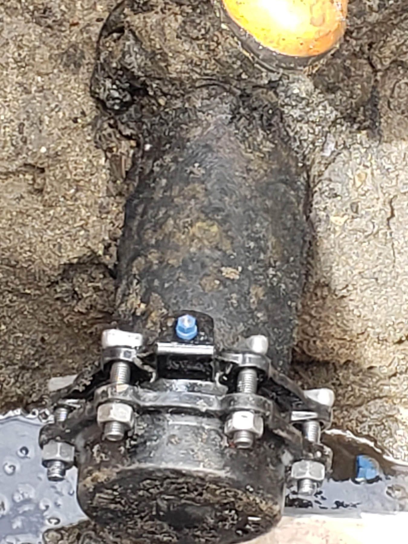 Black pipe section with flange connected to a yellow pipe, set in concrete, with water around the base.