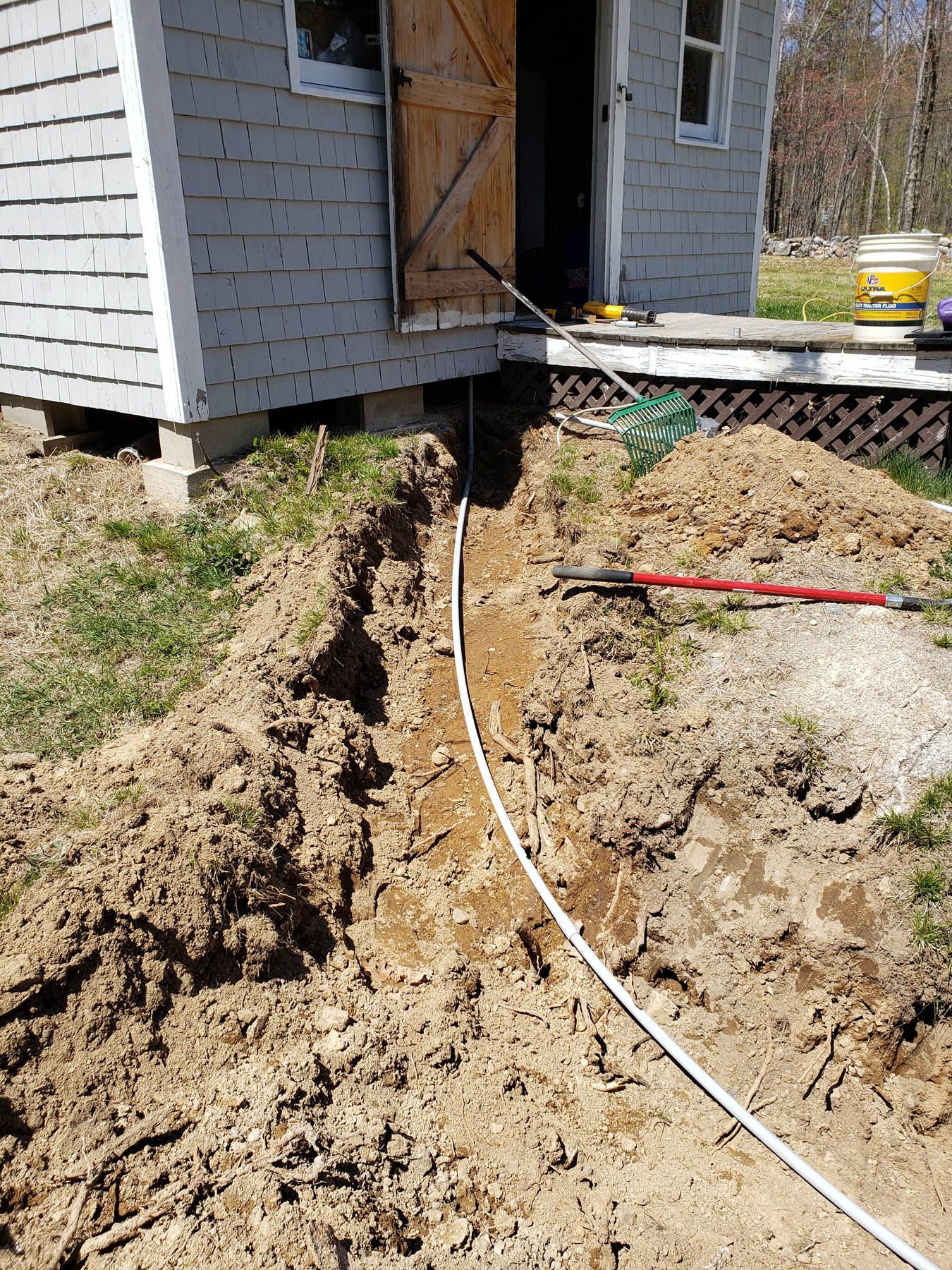 A trench dug next to a small building, with a white cable running through it.