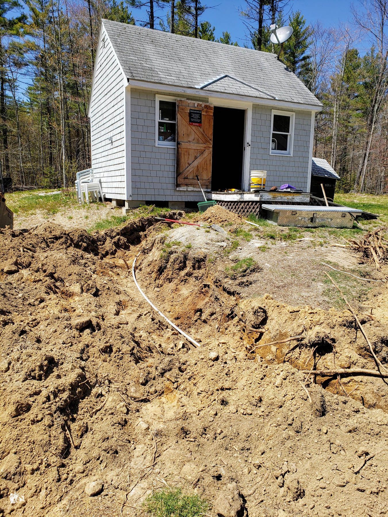 Small gray building with dirt mound in front, a white cable exposed in the dirt.