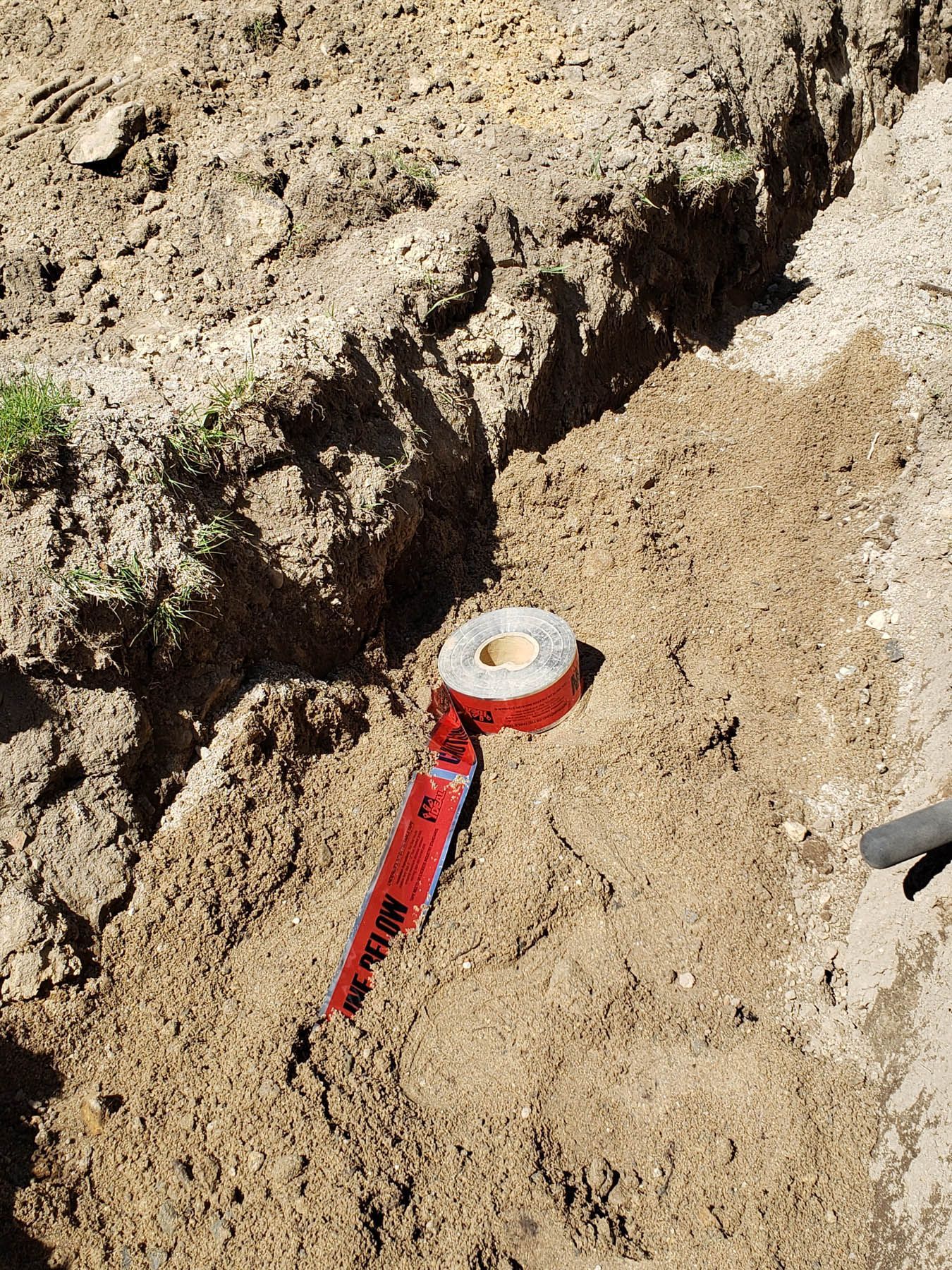 Trench in dirt with red warning tape.