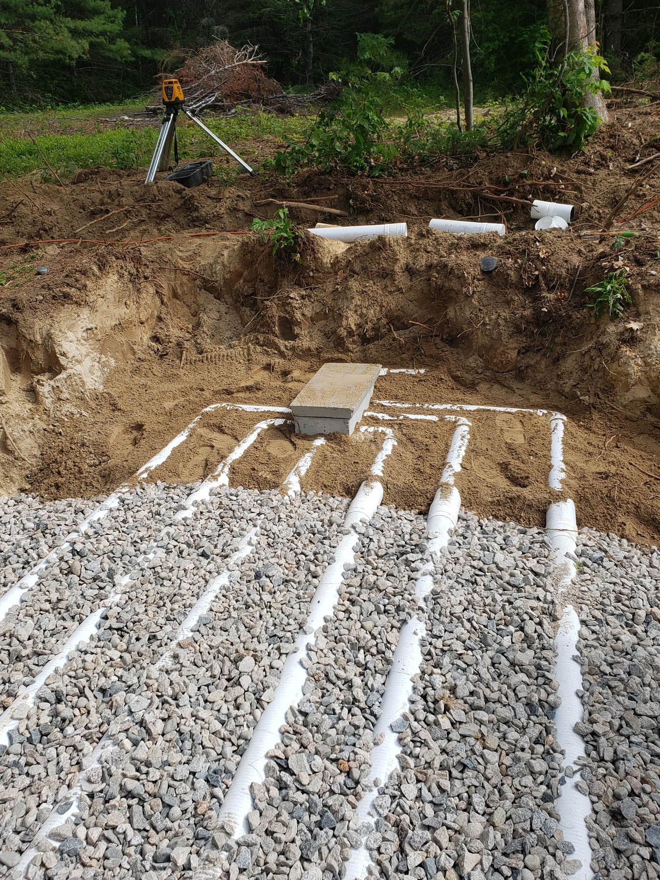A constructed septic system, gravel, white pipes, dirt and grass, outdoors.