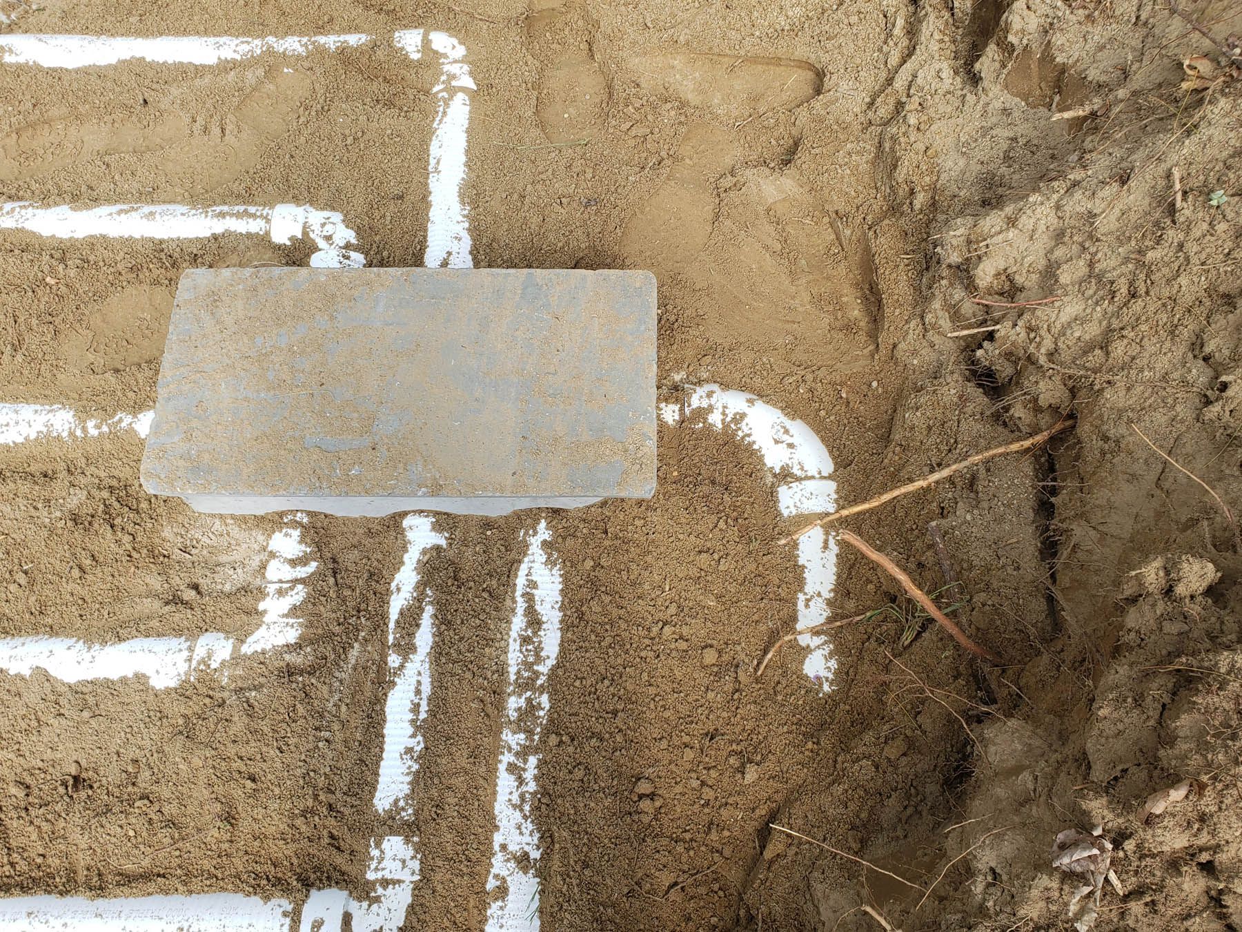 White pipes and a rectangular brick buried in sand.