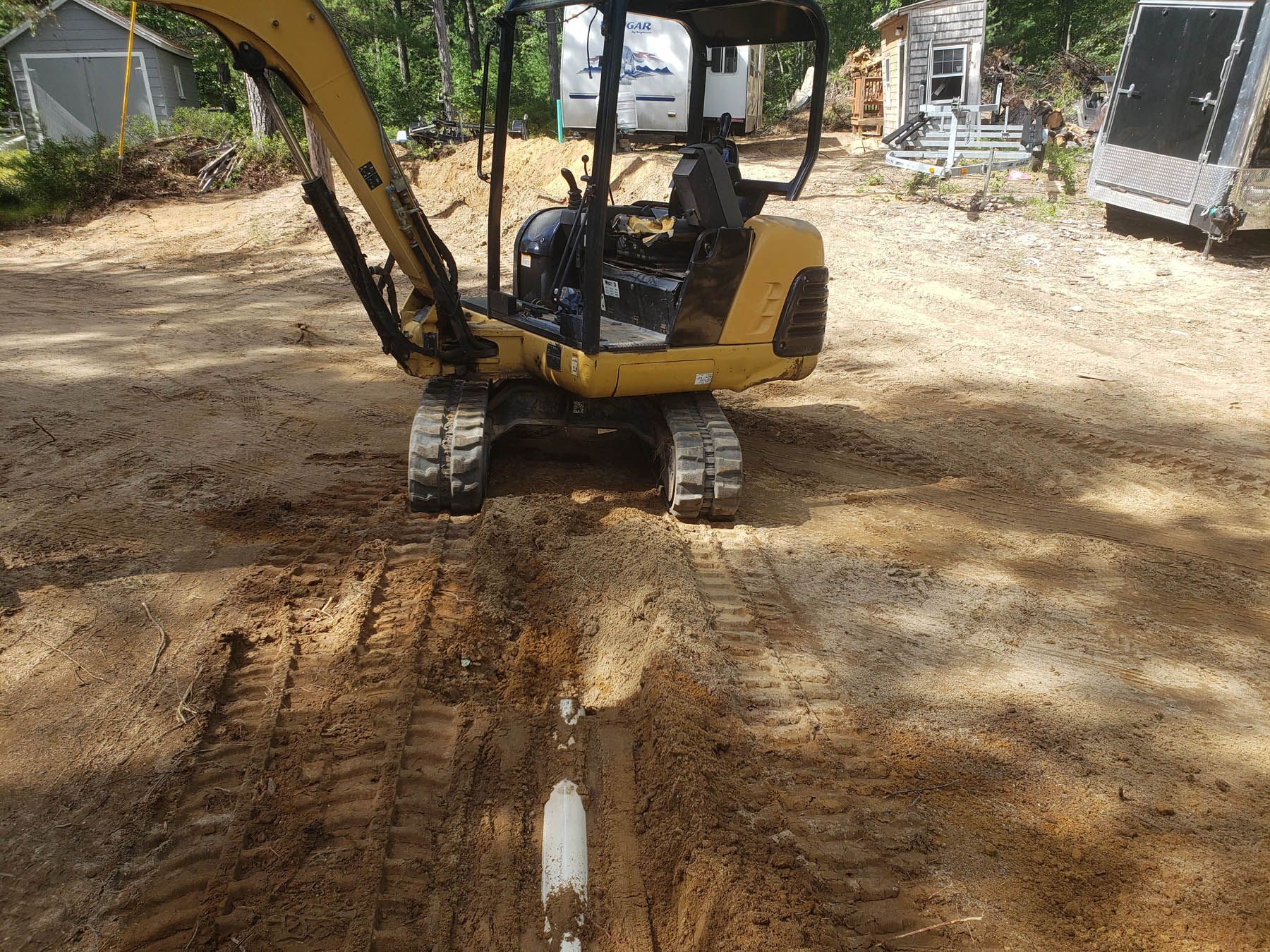 Yellow excavator digging a trench in sandy soil.