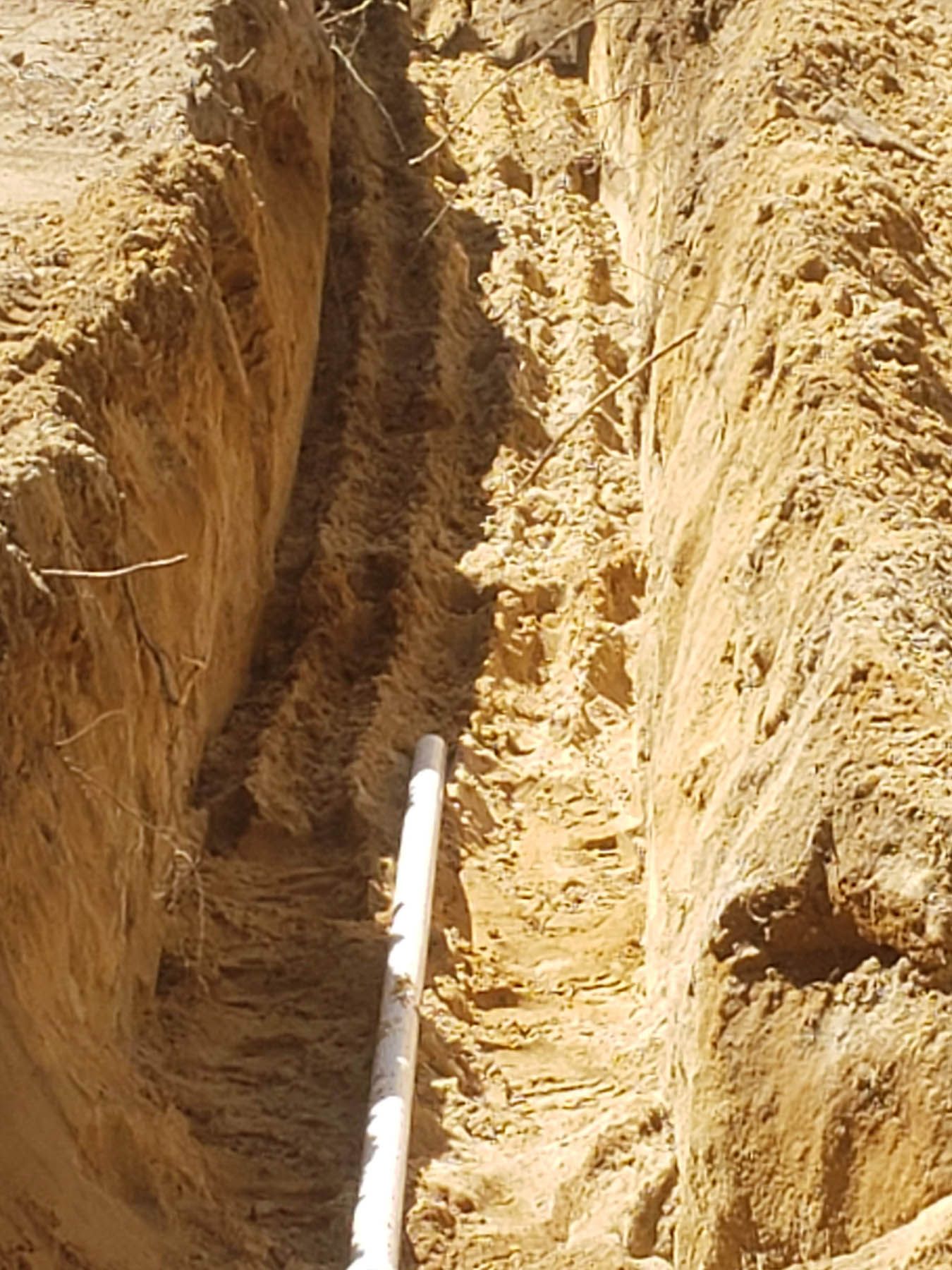 A trench in sandy soil with a white pipe extending down.