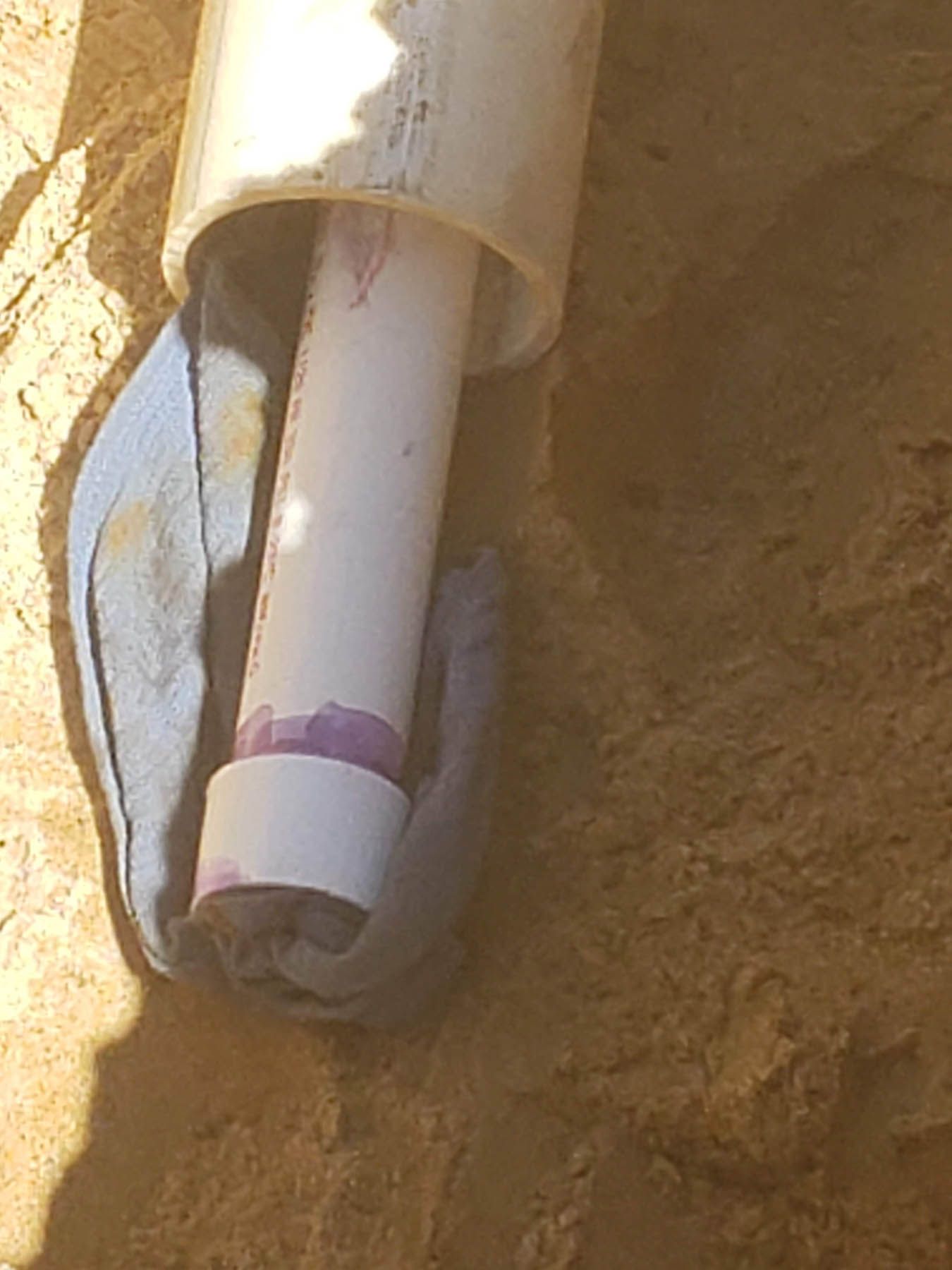 Gloved hands holding white PVC pipes in a sandy area, one pipe inserted into another.