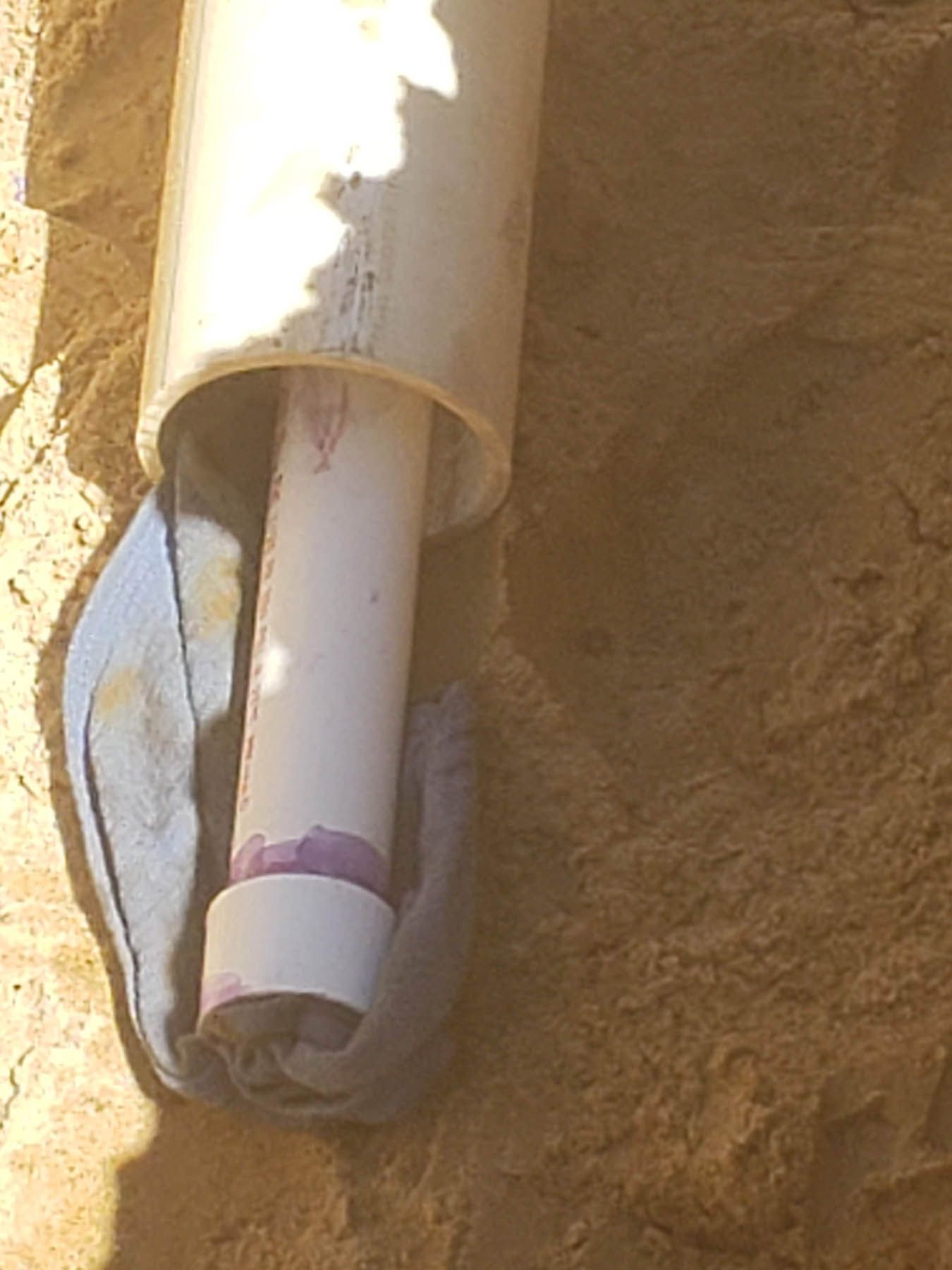 White PVC pipes being fitted together in a sandy trench, purple primer visible.
