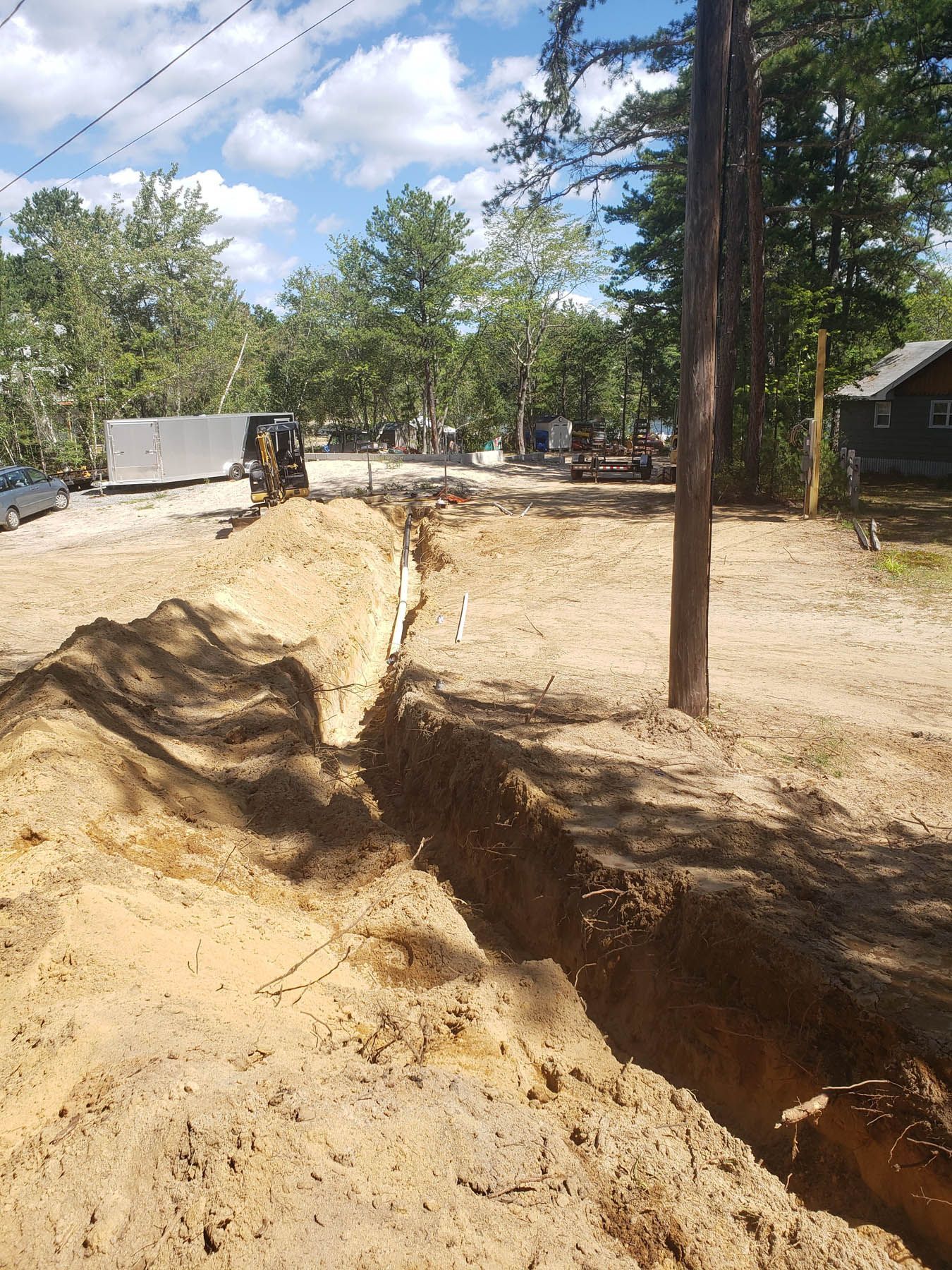Long trench dug in sandy soil, a utility pole and trees nearby.