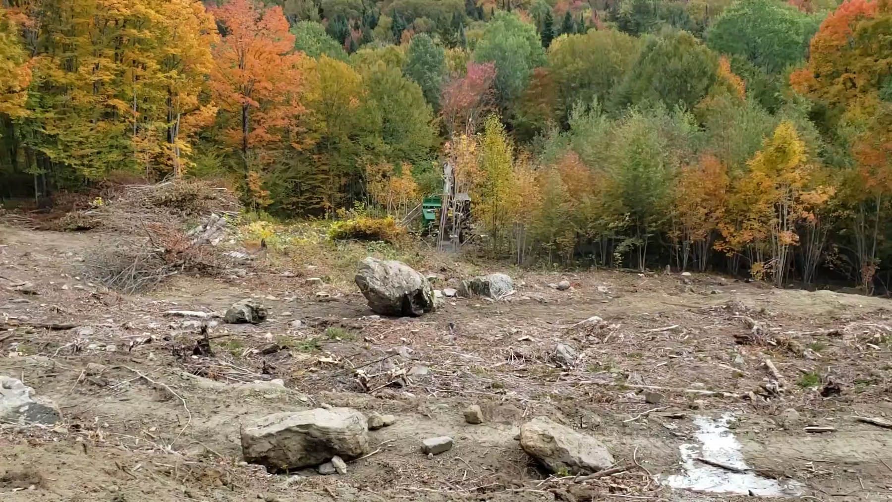 Cleared land with rocks in foreground, colorful autumn trees in background.