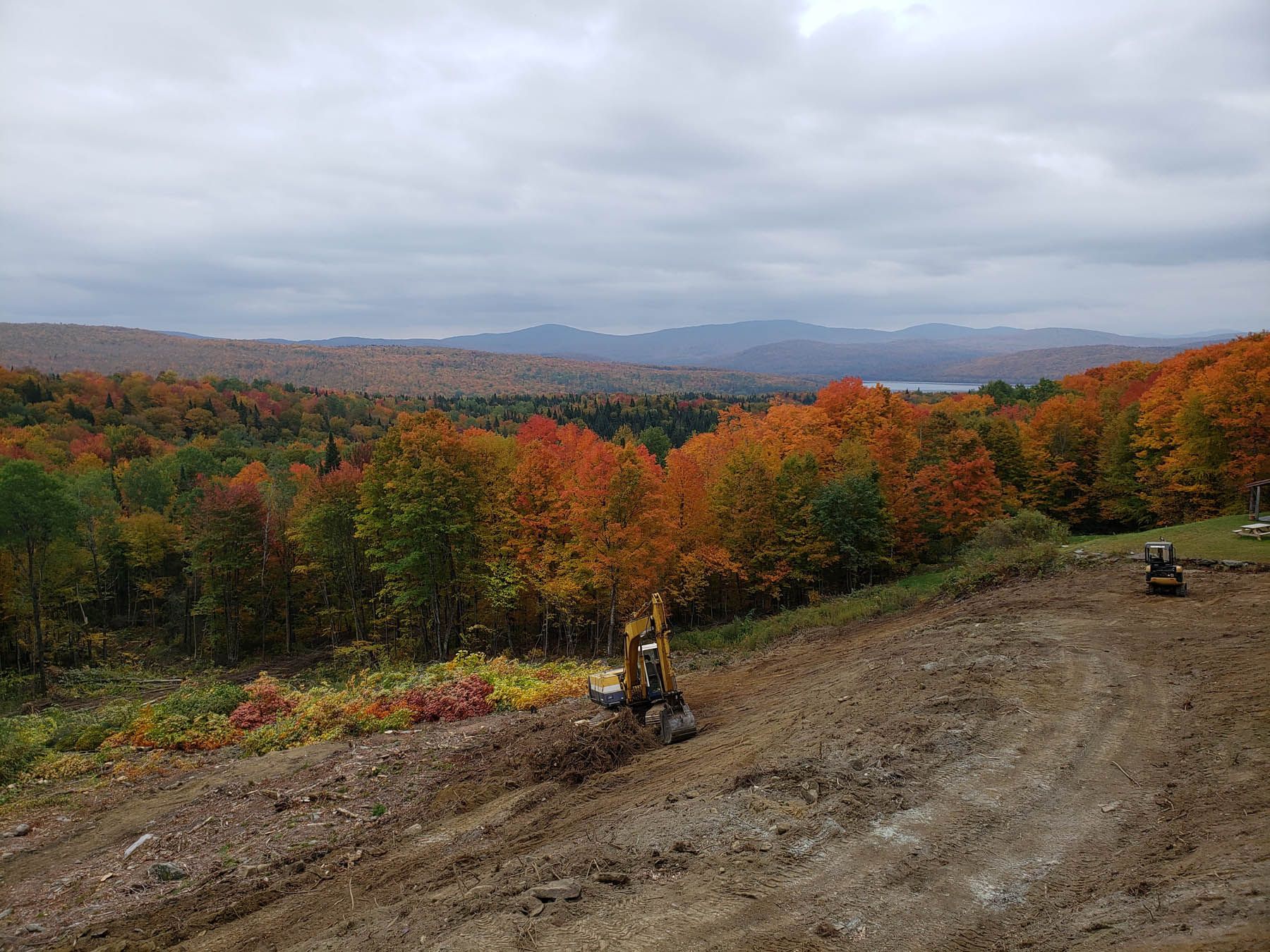 Construction site overlooking a vibrant autumn forest; cloudy sky.