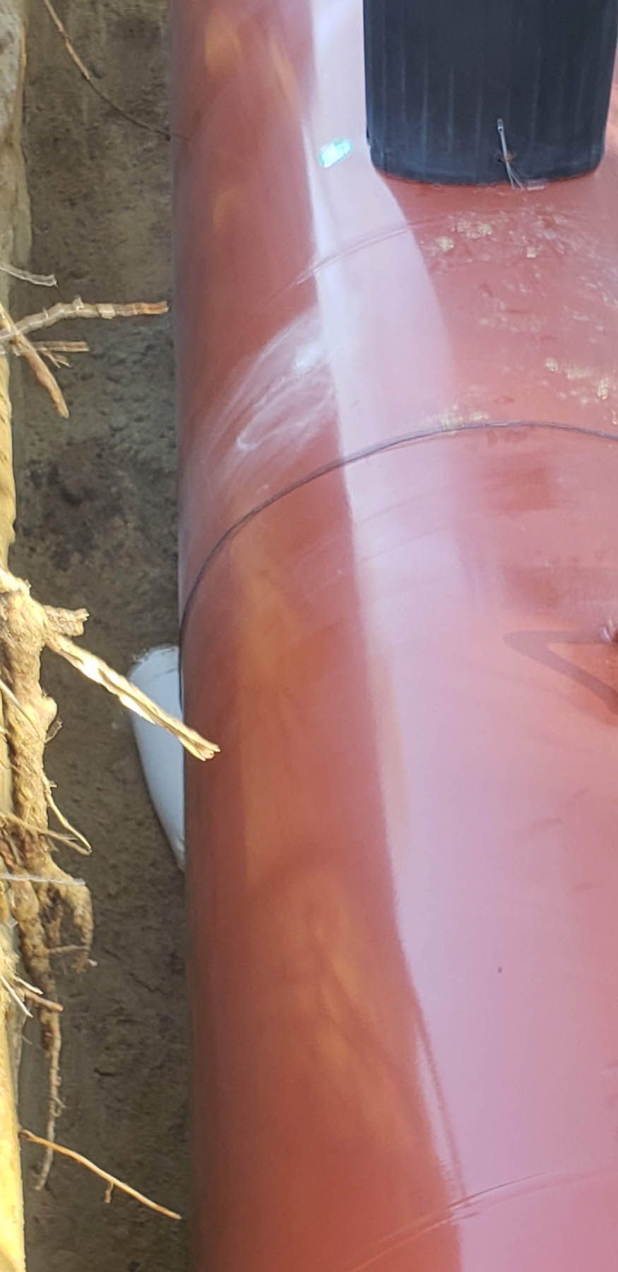 Red pipe in a trench with dirt and a black pot.