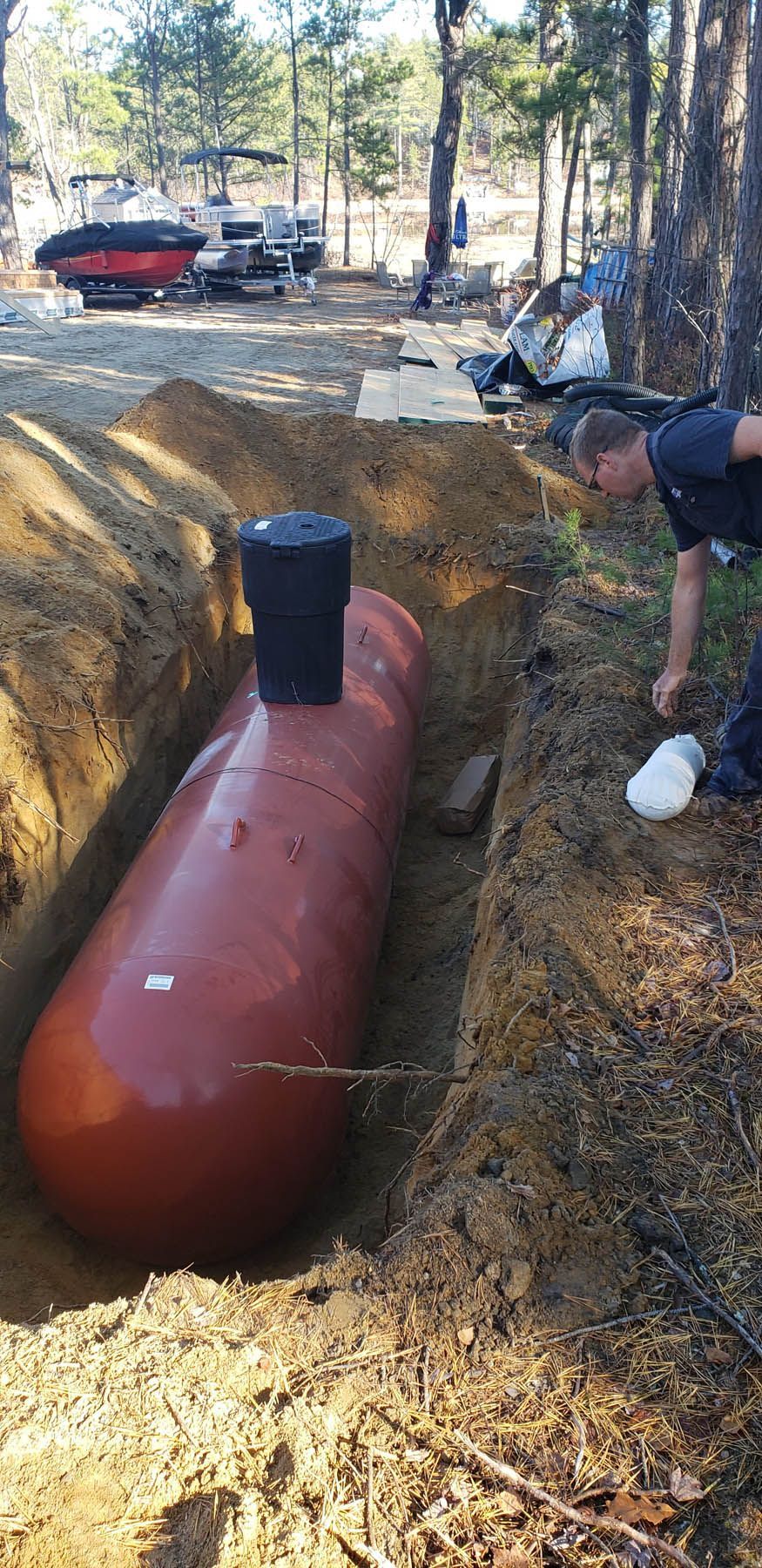 Red propane tank in a trench, being inspected by a person in a wooded area.