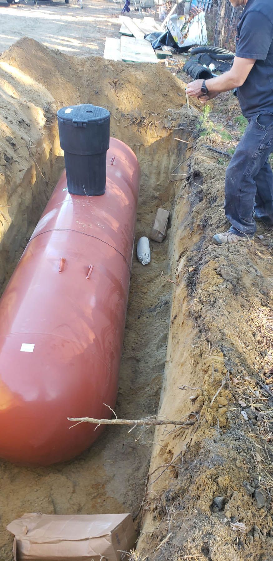 A large, reddish-brown propane tank being installed in a trench, next to a person.
