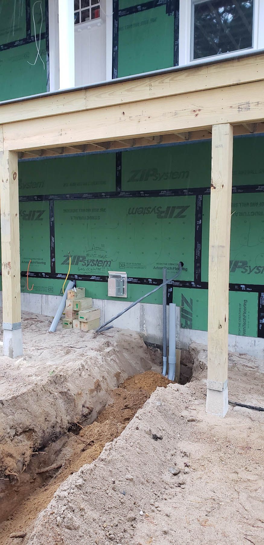 Construction site with a trench, wood posts, green wall, and a building.