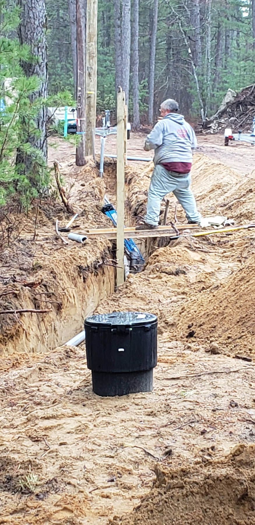 Man working on a septic system in a forest. A black tank is in the foreground.