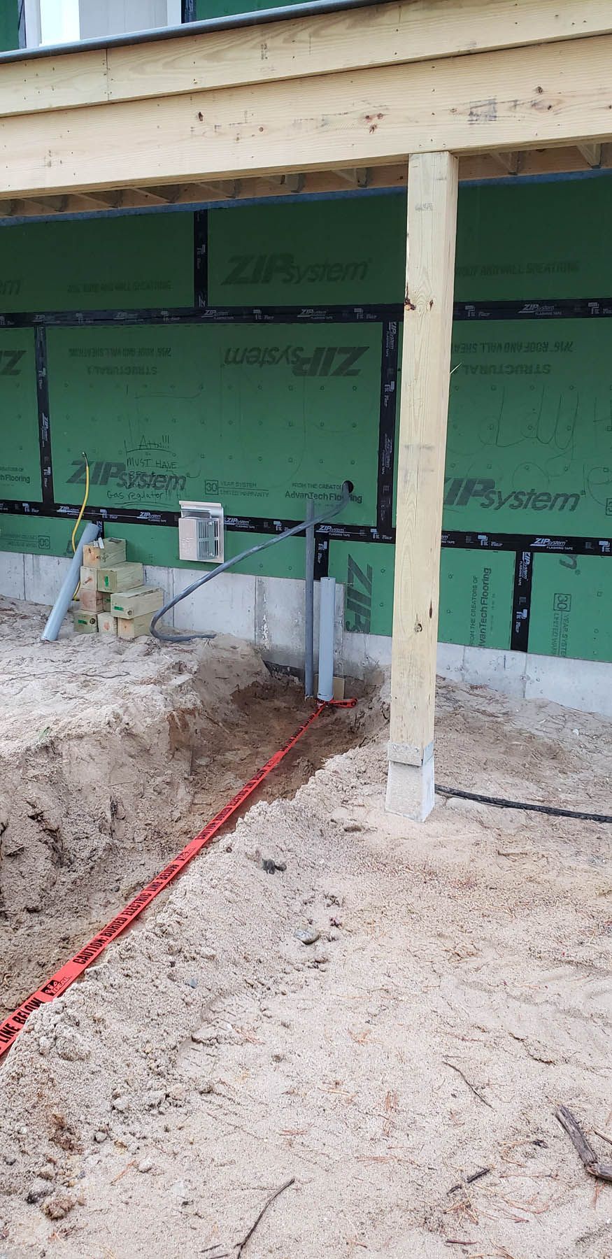 Construction site with trench and red wire running to a box on a wall.