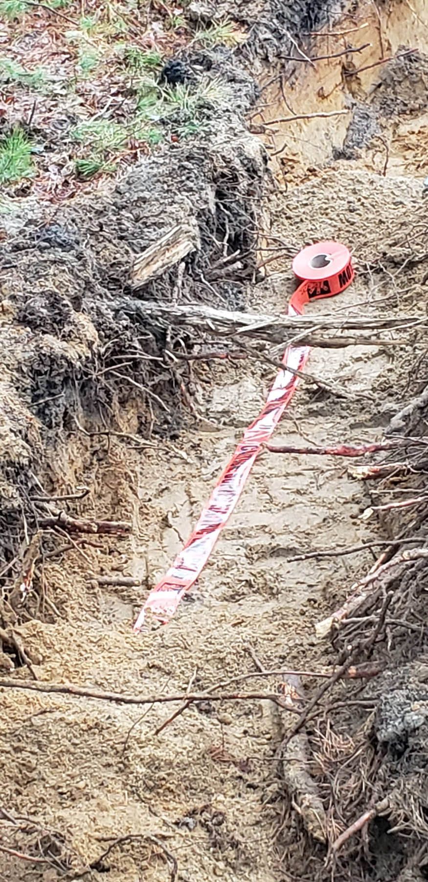 Red and white surveying tape hangs down a ditch in a brown soil bank.