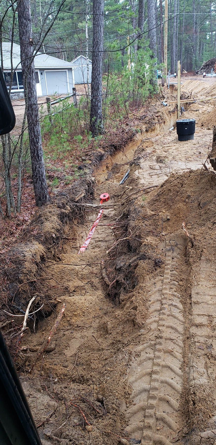 Dirt work in progress, with an excavated trench marked by a red line, flanked by trees and a building.