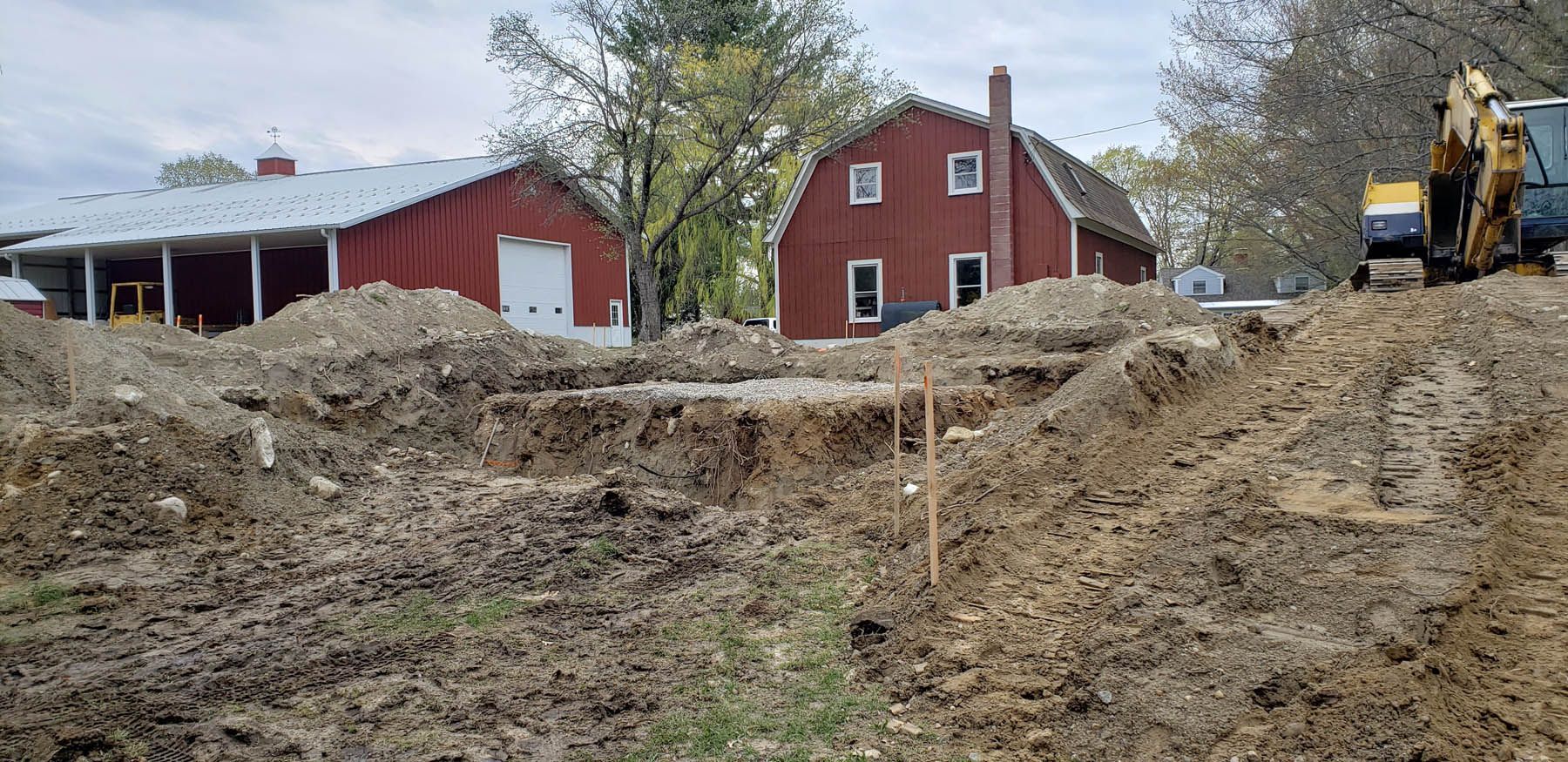 Construction site with red buildings, a pile of dirt, and an excavator.