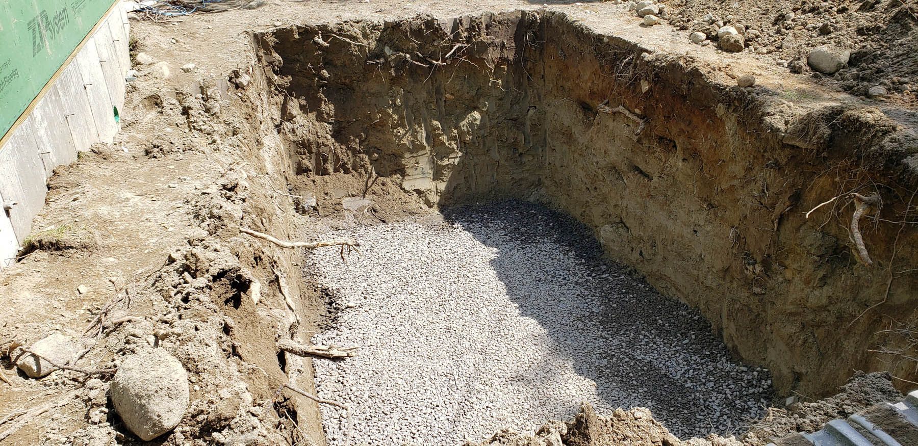 A rectangular hole in the ground filled with gravel, next to a concrete structure.