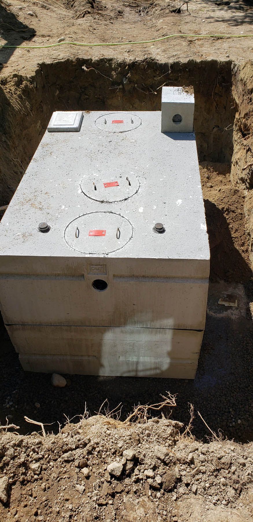 A concrete septic tank in a hole, surrounded by dirt.