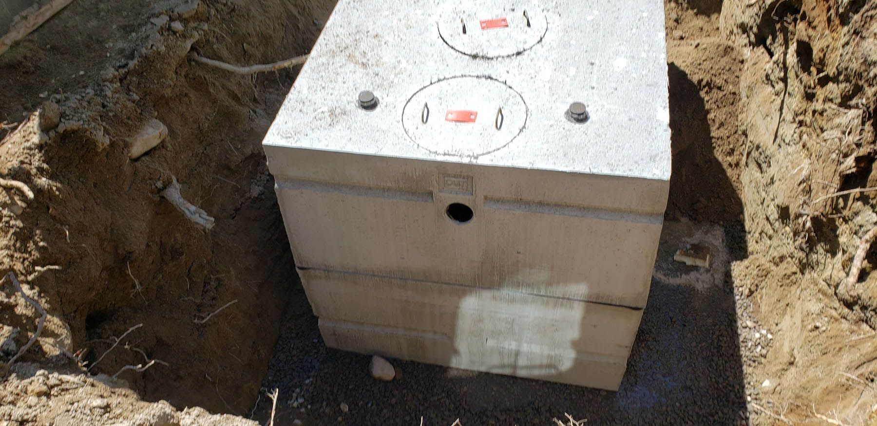 A concrete septic tank in a freshly dug pit. The top has two circular access points.