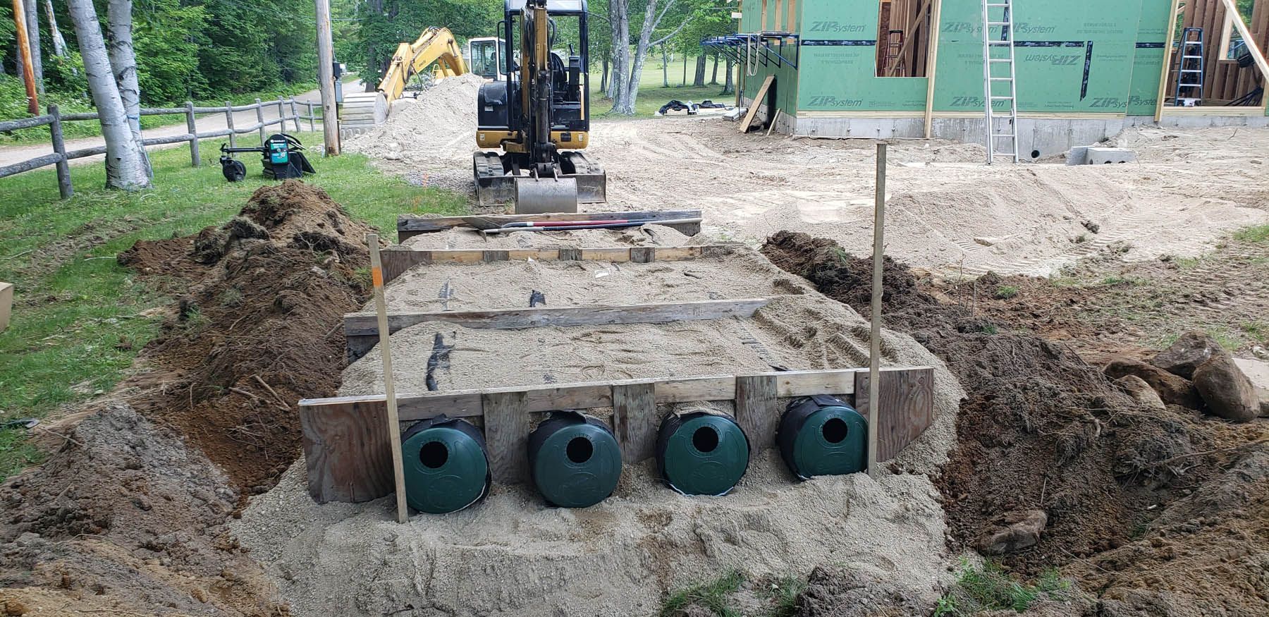 Construction site with an excavator, green tanks, and a house under construction.