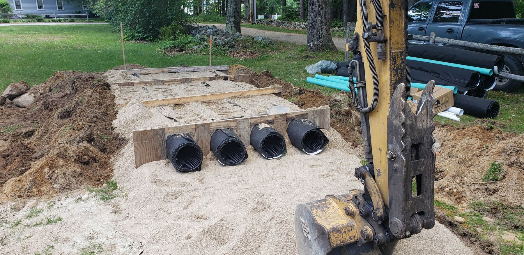 Construction site with an excavator and four black pipes in a gravel trench.