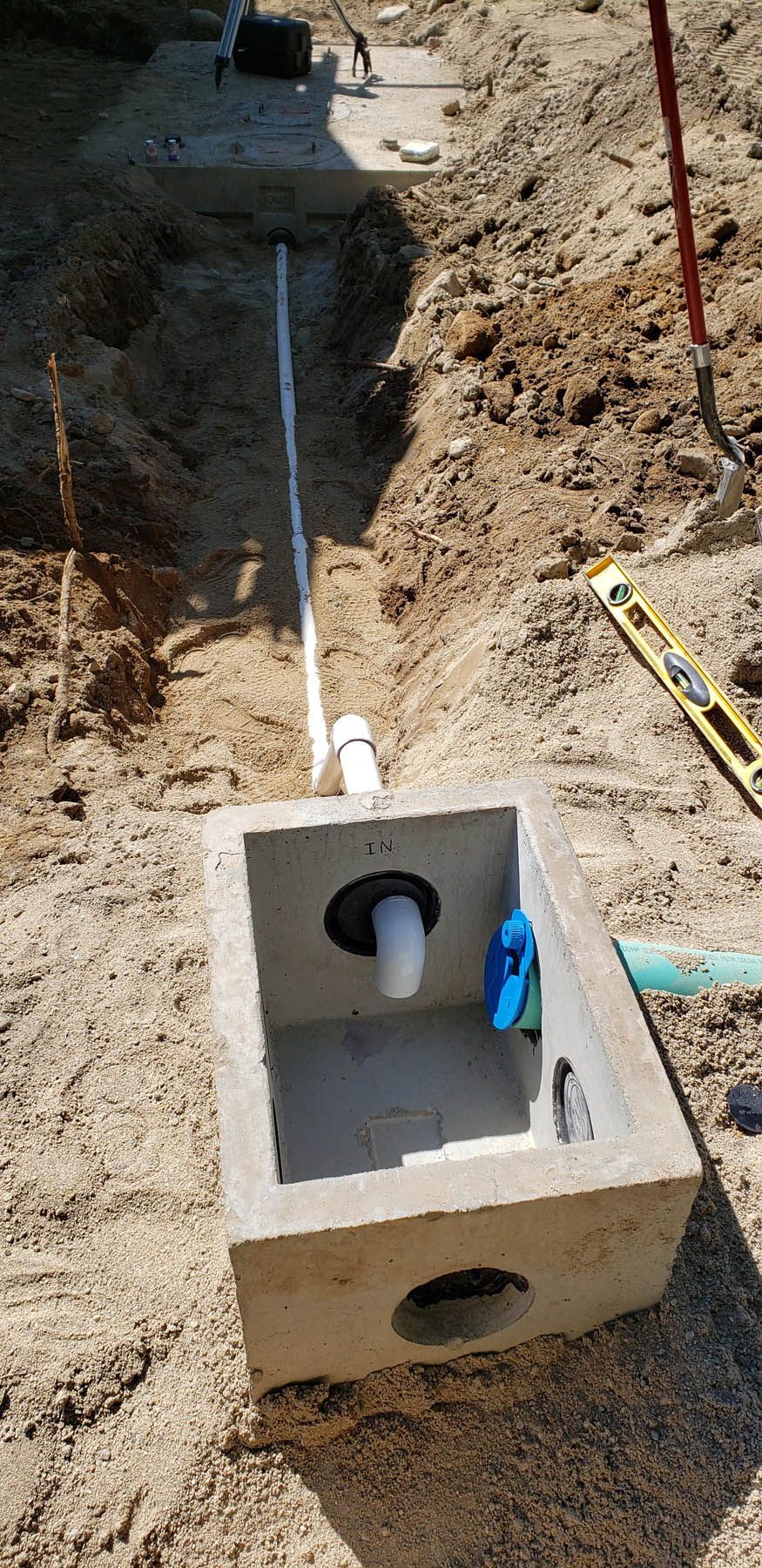Concrete box with white pipe connections in an open trench, earth background. Construction.