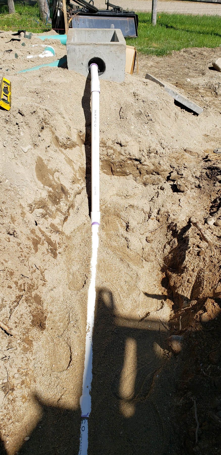 A white pipe in a trench connected to a concrete block, in a construction site.