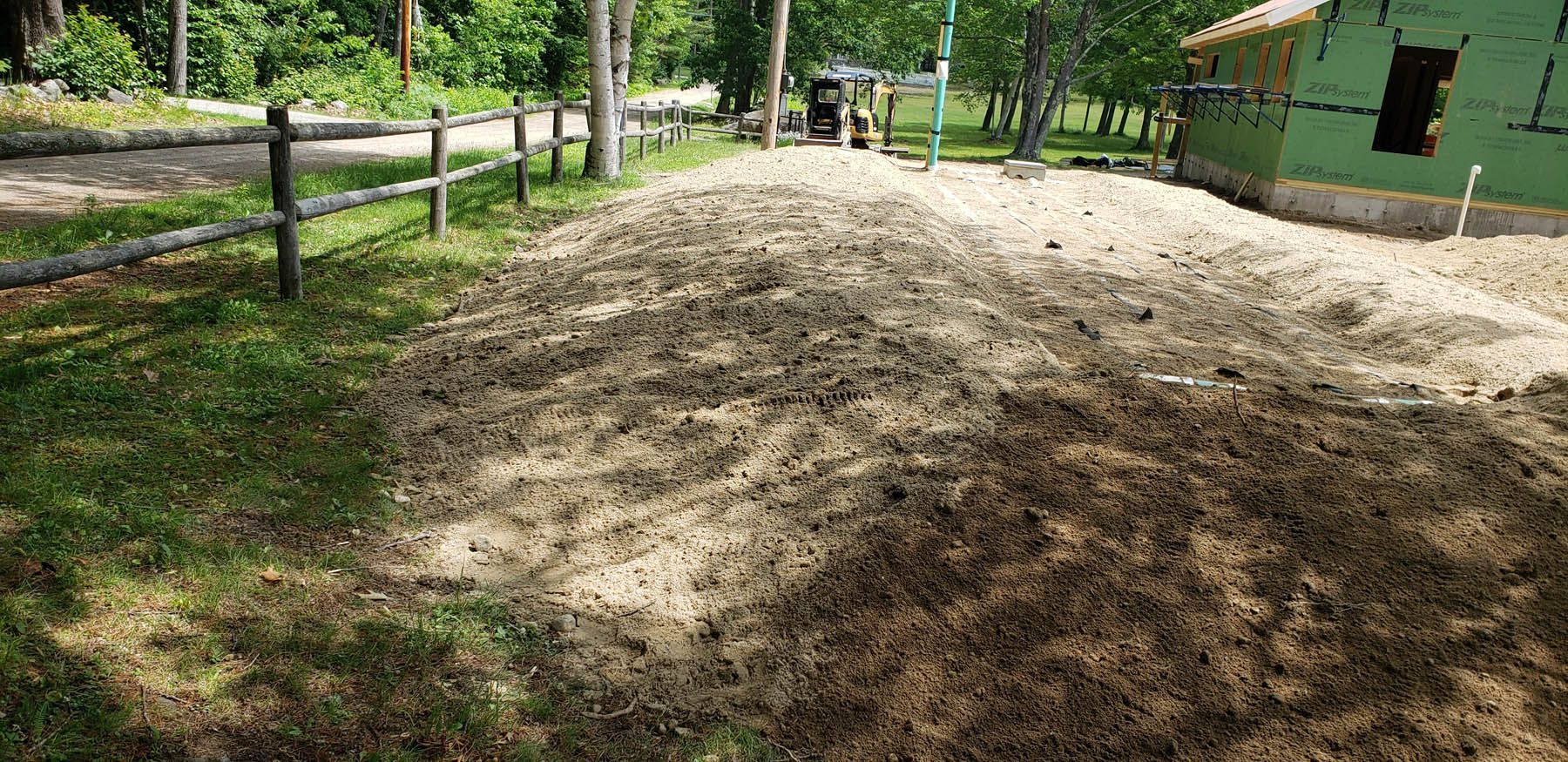 A sandy area with patches of grass, trees, and a building under construction.