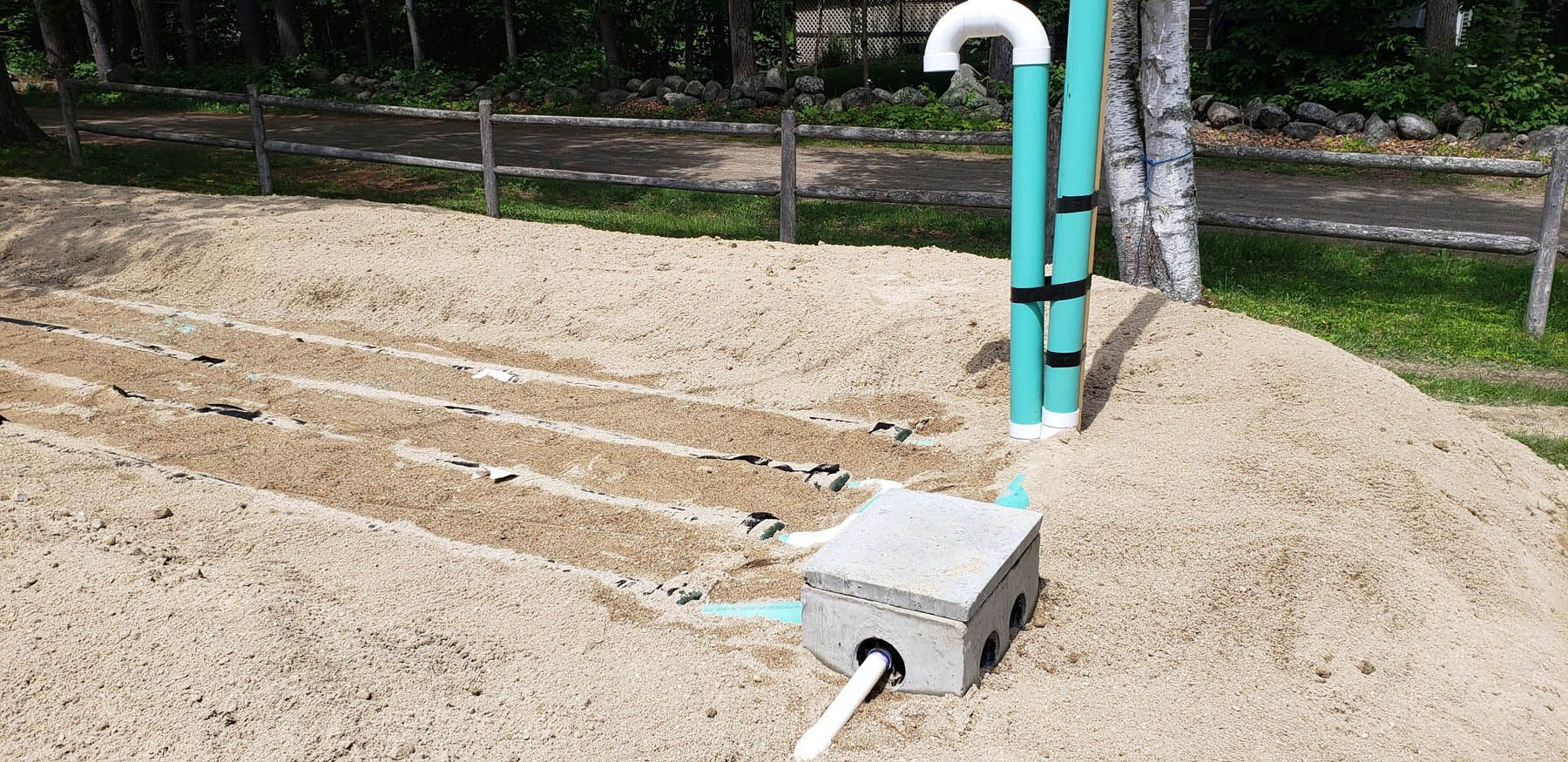 A constructed sand filter with pipes and a control box in a backyard setting.