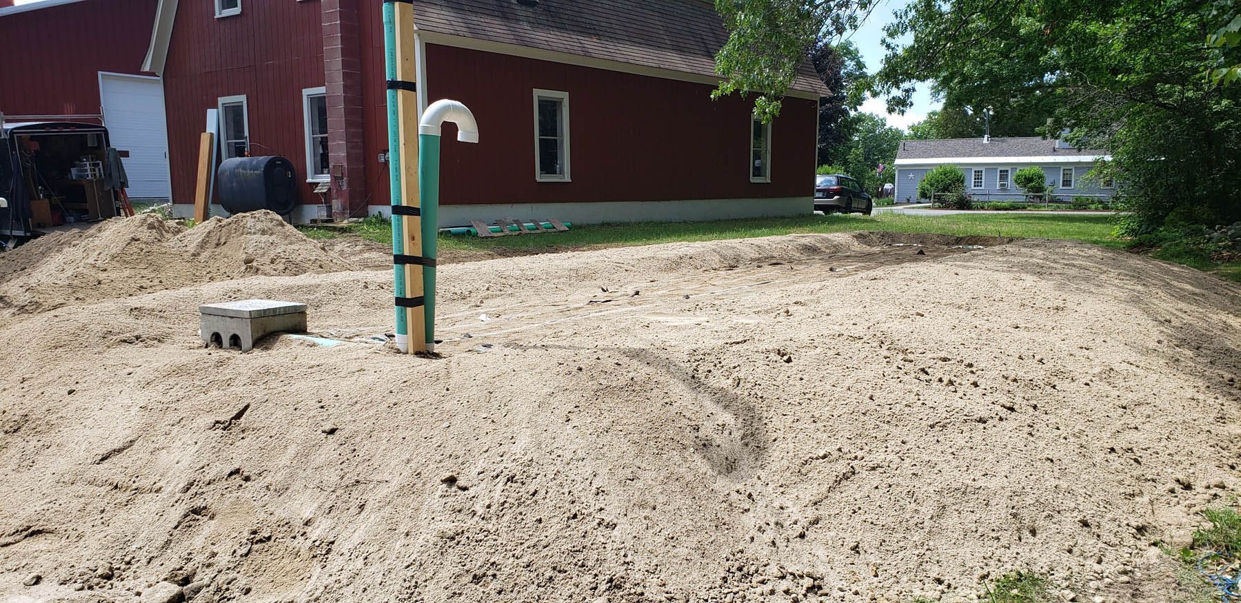 A dirt field with a red building in the background and piping in the center.