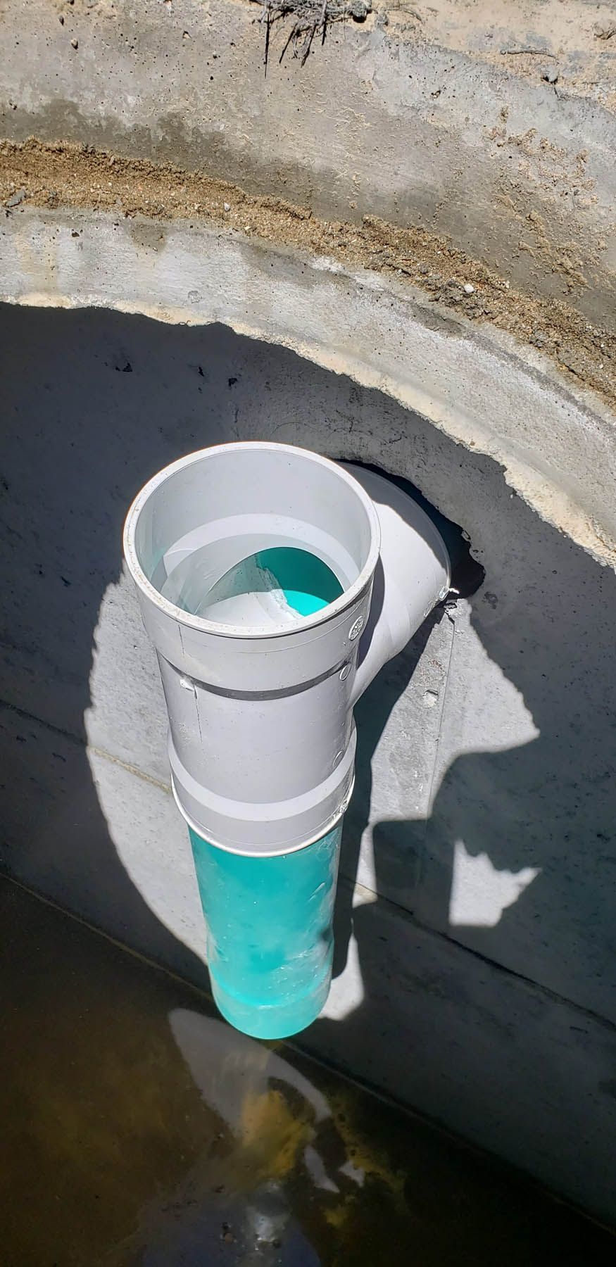 A concrete drainage pipe with a white and teal pipe sticking into it, partially submerged in water.