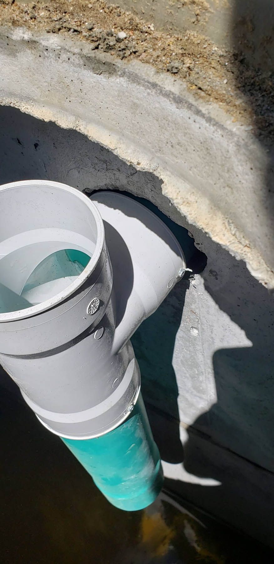 Gray and teal PVC pipes drain into a concrete gutter with water inside.
