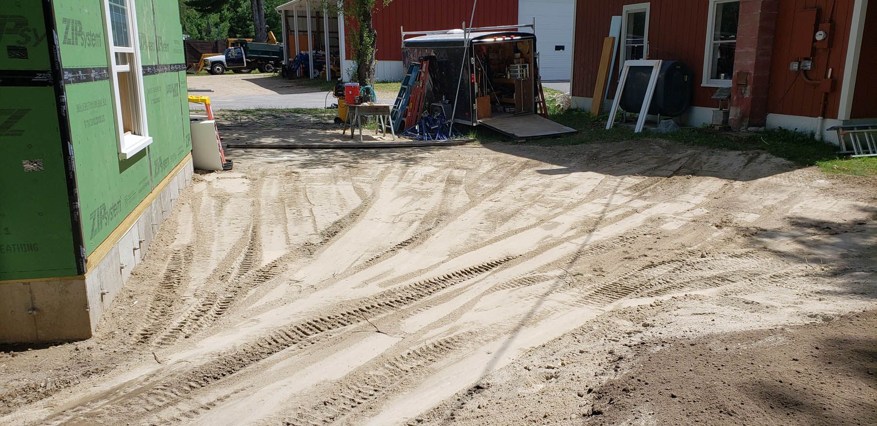 Construction site with a dirt ground and tire tracks next to a building.
