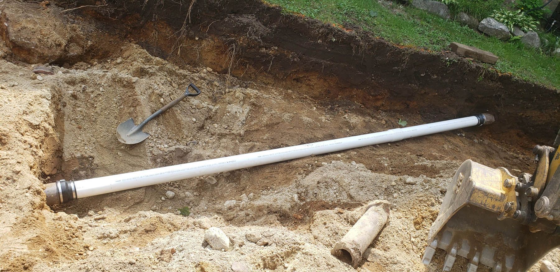 A white PVC pipe in a trench with a shovel and small construction equipment.
