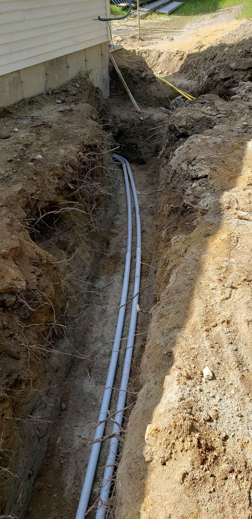 Trench with buried PVC pipes next to a building.