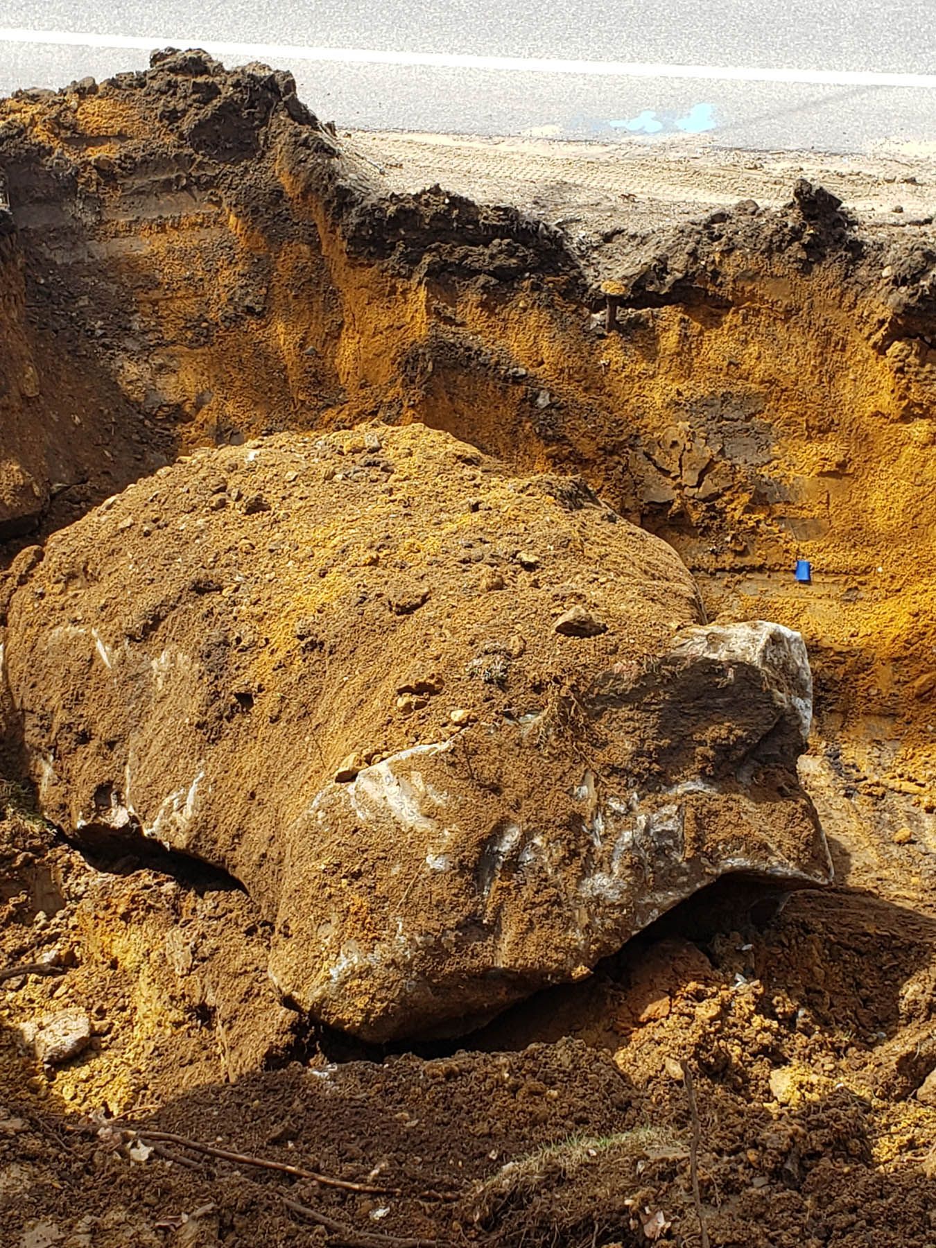 Large, unearthed boulder covered in dirt, within a construction site with exposed yellow-brown soil.