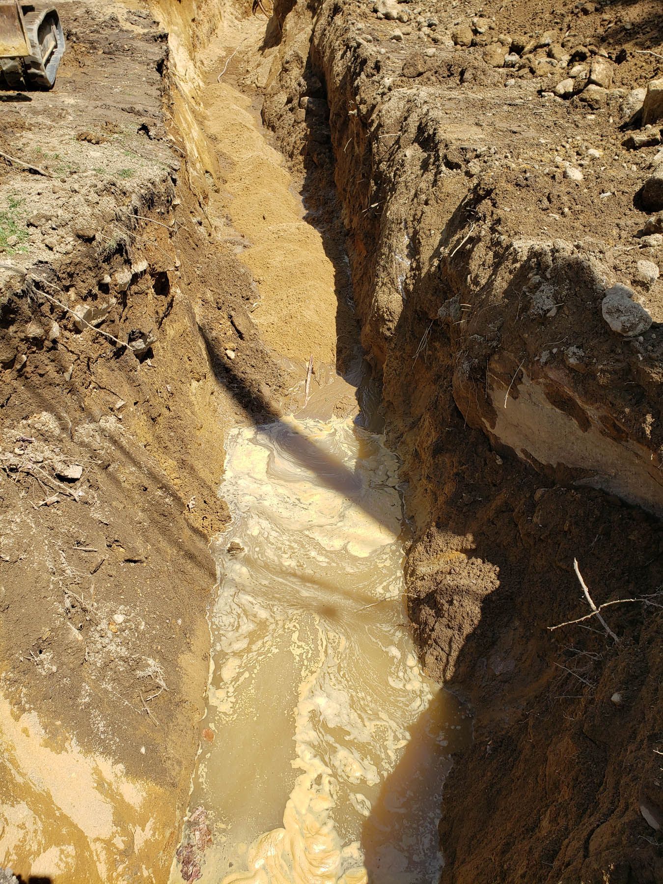 A long, muddy trench filled with water, dug into dirt.